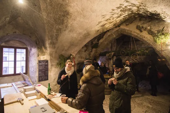 People enjoying food and drinks inside a rustic vaulted cellar with stone walls
